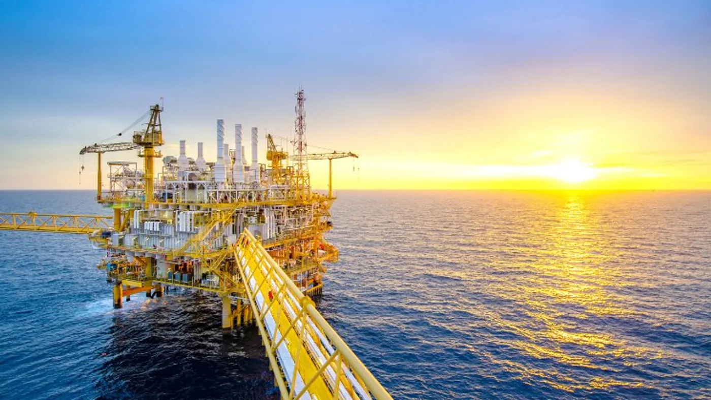 Plataforma de petróleo offshore ao pôr do sol, com passarela de acesso sobre o mar