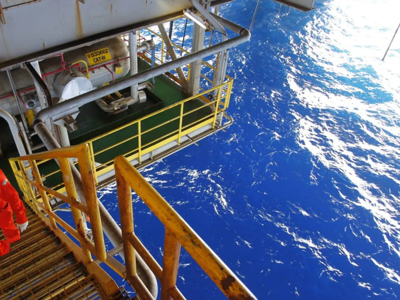 Profissional com macacão e capacete em escada de acesso de plataforma offshore sobre o mar